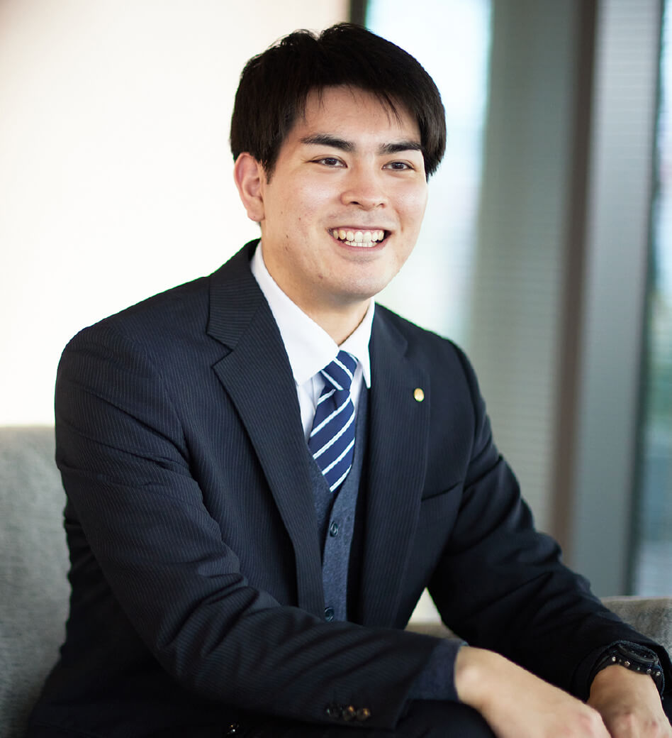 画像:K.U.さん、笑顔でソファに座っている。