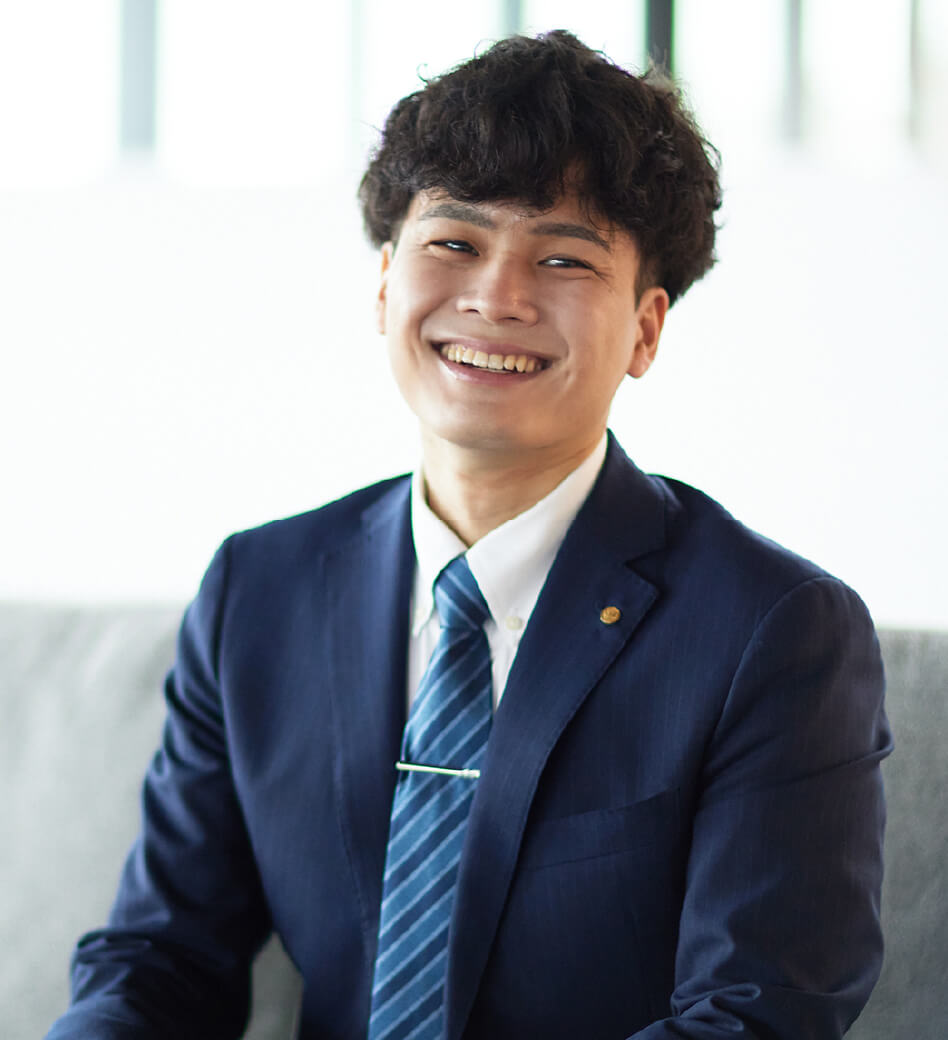 画像:S.A.さん、スーツ姿でソファに座る、笑顔の様子。