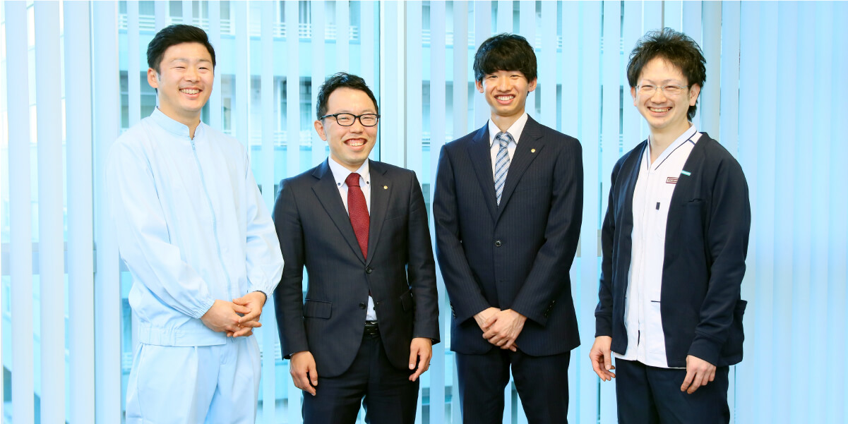 画像:ビルの窓際、4人並んで笑顔でいる様子。